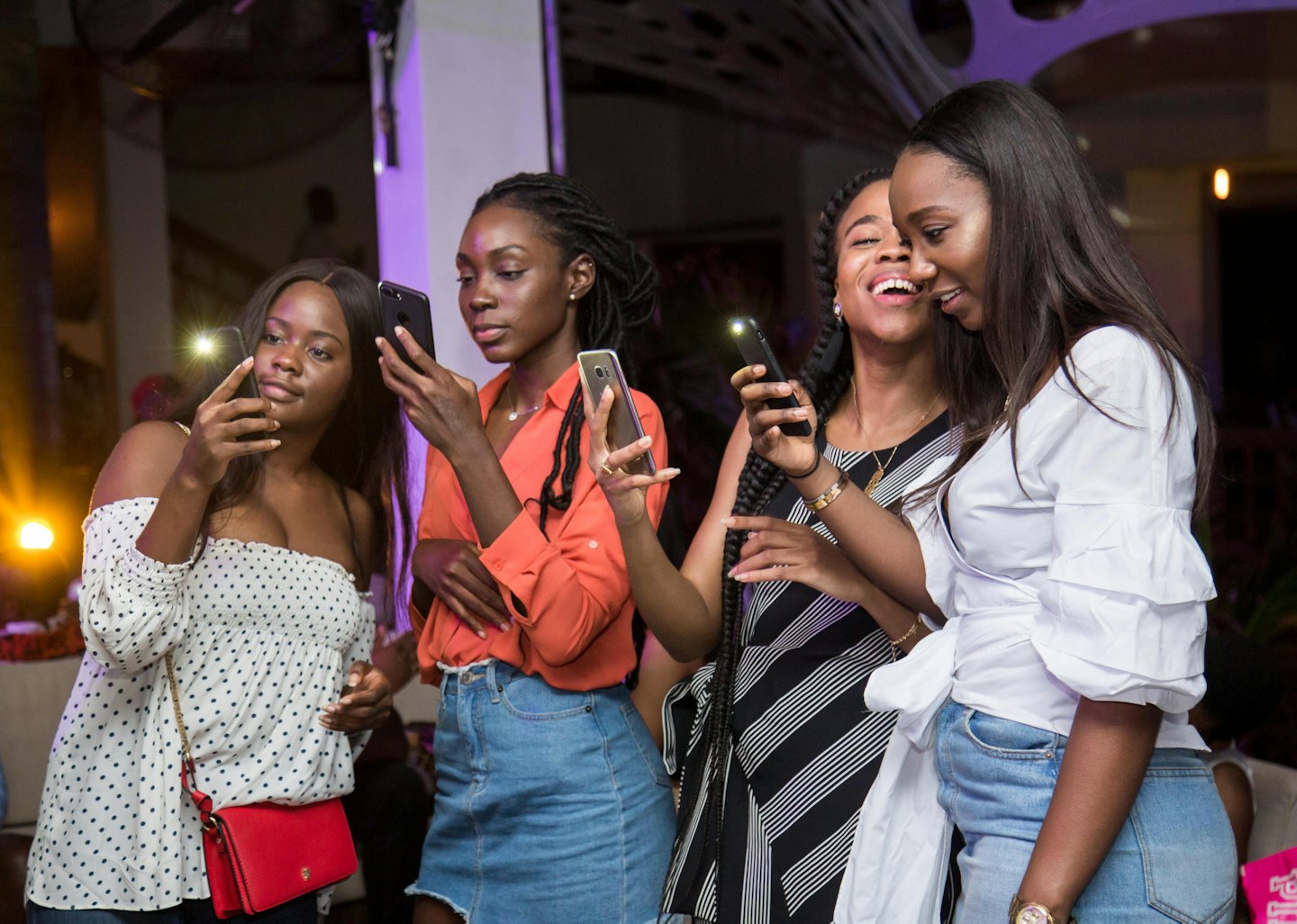 Four women use smartphones at a dimly lit event.