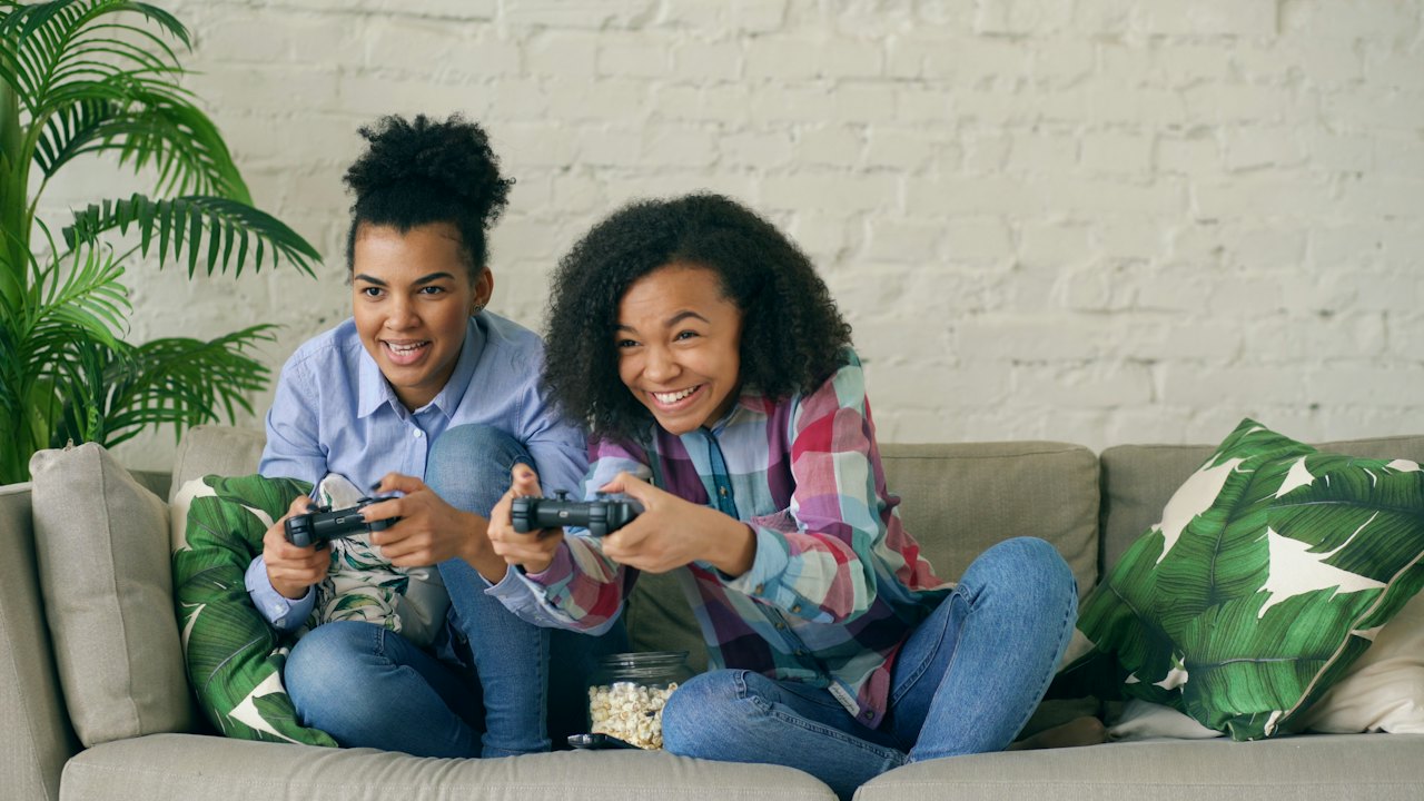 Two young women enjoying a gaming session on a couch, holding game controllers and smiling.