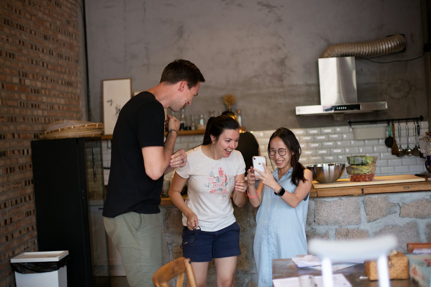 Three friends laughing together while looking at a smartphone.