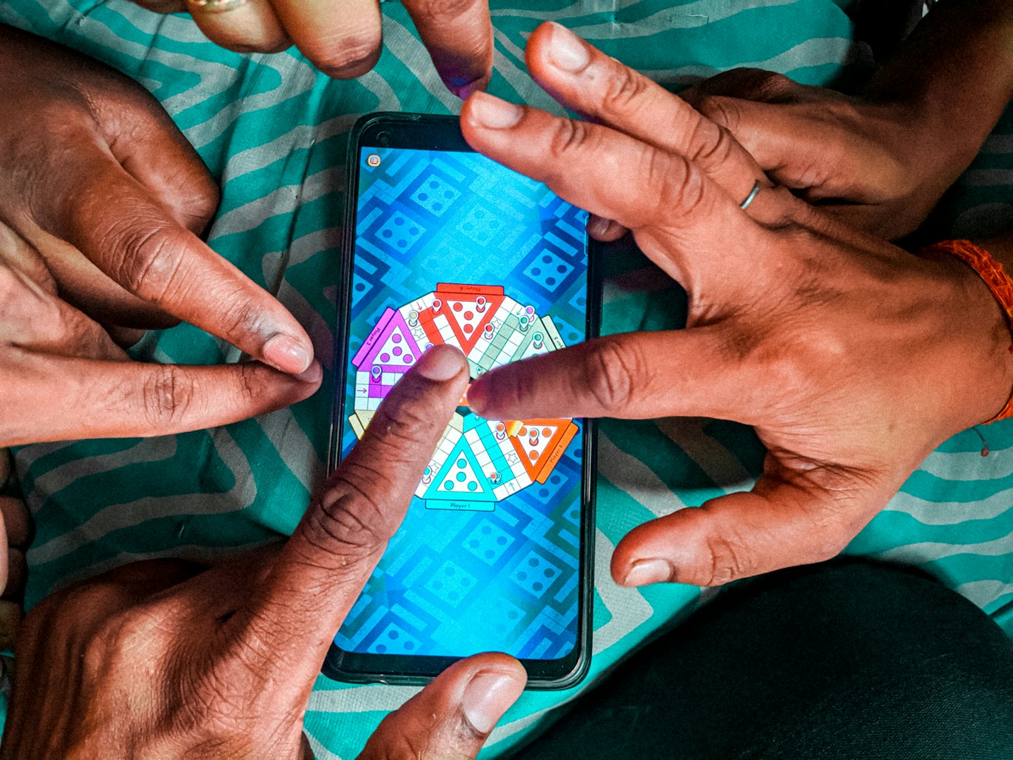 Several hands play a colorful digital board game on a smartphone.